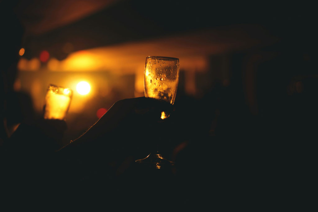 A silhouetted hand holds a champagne flute against a warm, glowing background at an evening celebration.
