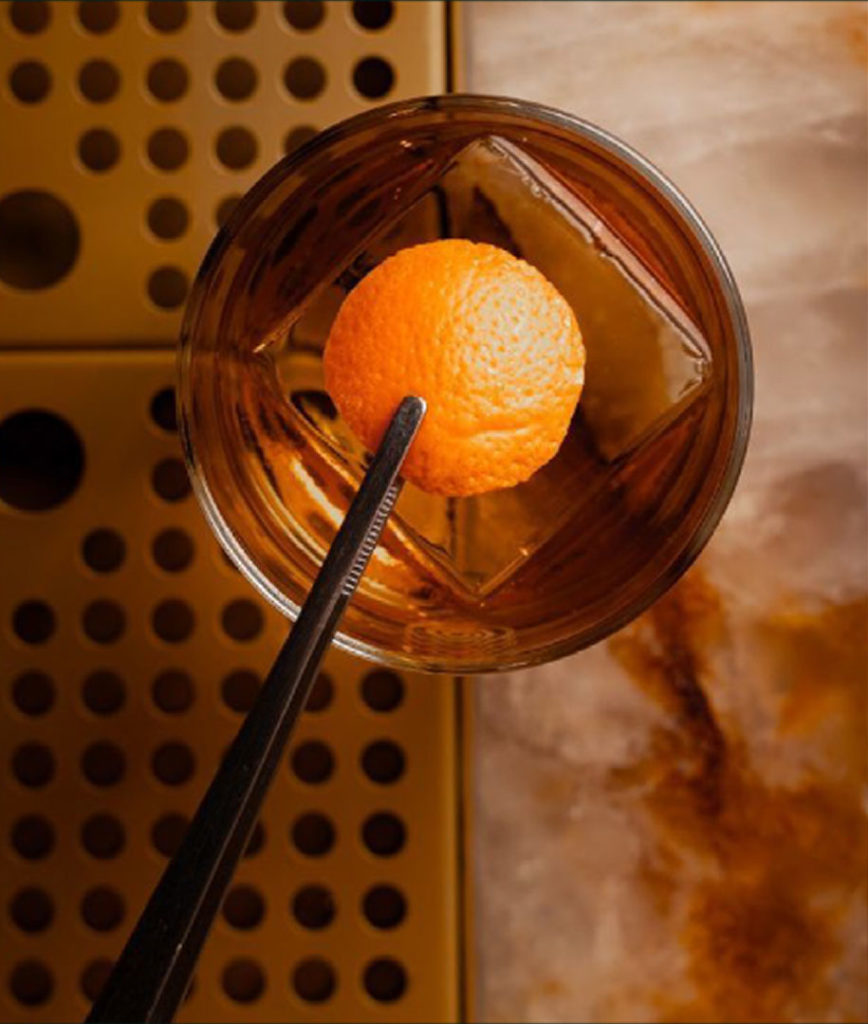Orange peel in cocktail glass with ice, top view on marble bar counter.